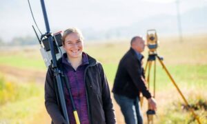 Licensed land surveyor using GNSS receiver in the field with teammate operating total station