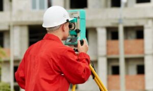 Professional land surveyor using a total station in front of a commercial building, performing an ALTA Survey to gather property boundary data