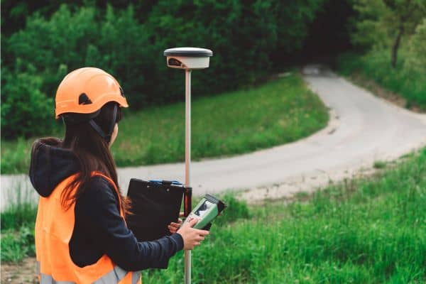 Surveyor performing a topographic survey on rural land near a gravel road to assess drainage and grading in 