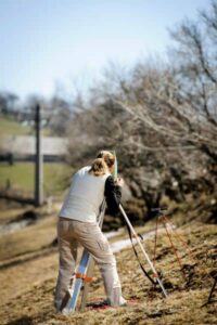 Land surveyor using equipment on sloped terrain to measure horizontal and vertical accuracy for reliable topo surveys in Bowling Green

