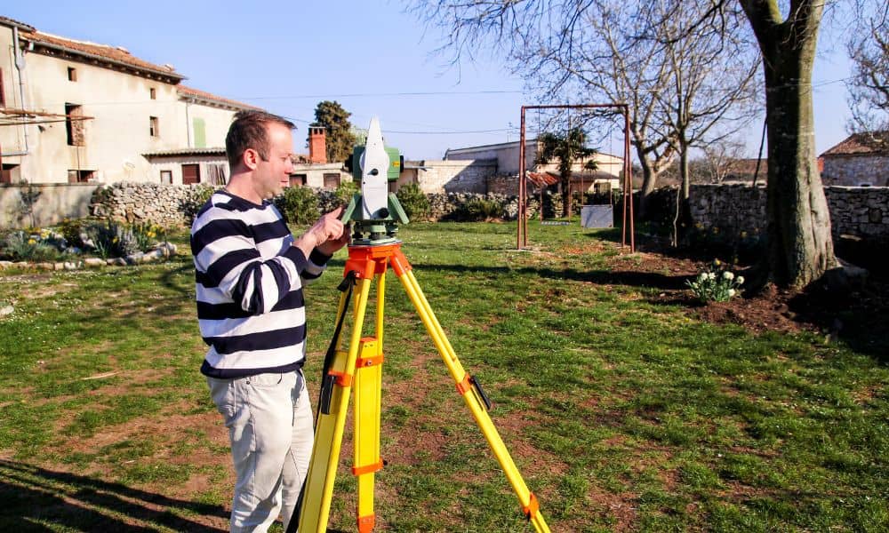 A licensed land surveyor measuring a home’s elevation to prepare a flood elevation certificate for lowering insurance costs