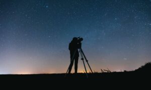 Land surveyor using tripod equipment under a starry night sky showing how a geomagnetic storm can affect GNSS accuracy during a boundary survey