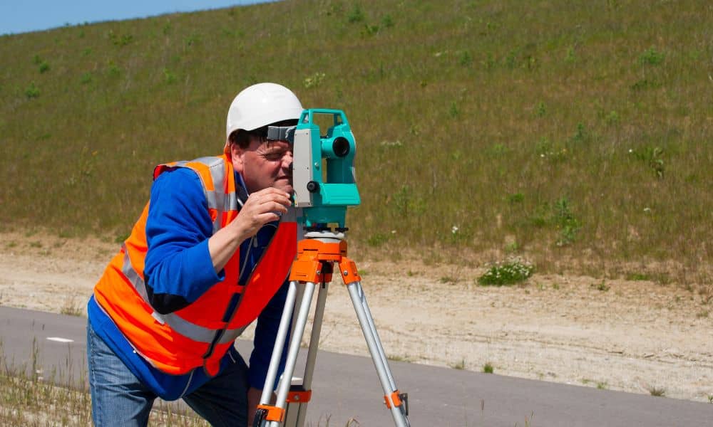 Land surveyor using a total station along a new public path project for an ALTA Land Title Survey.