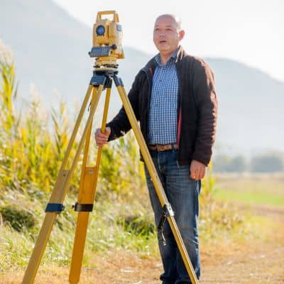 Surveyor using a total station to capture elevation details that support topo surveys and improve understanding of landslide risks