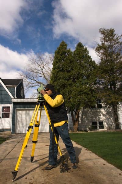 Land surveyor measuring a residential property line while determining property survey cost in a boundary dispute